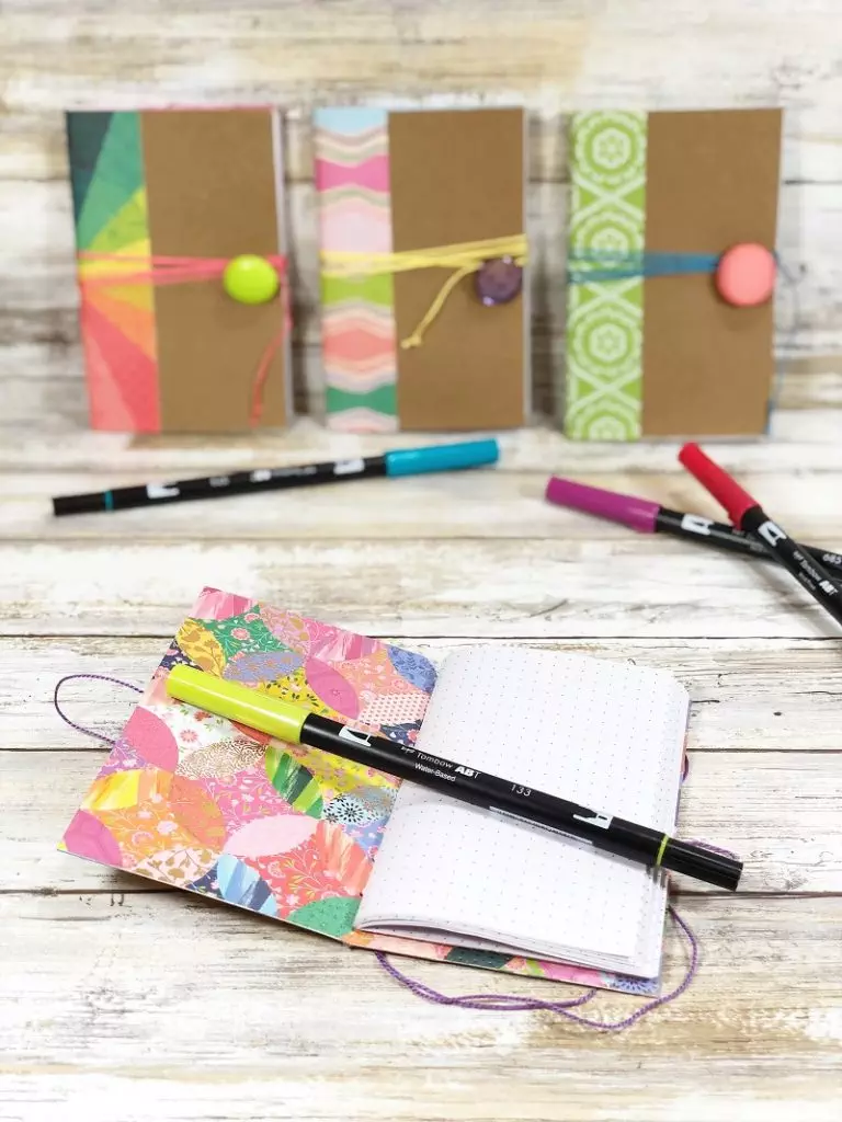 Four notebooks made from a recycled cereal box with colorful patterned paper and buttons #creativelybeth #recycled #crafts #notebooks #journals #upcycled
