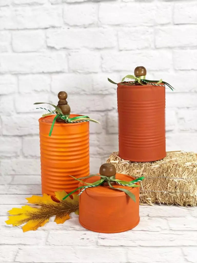 How to Recycle Tin Can Pumpkins for Autumn Creatively Beth Three orange cans sitting on a hay bale on a brick background #CreativelyBeth #recycledcrafts #fallcrafts #pumpkincrafts #autumncrafts